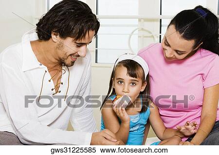 Close-up of a young couple looking at their daughter eating a pastry View Large Photo Image Stock Photography - Close-up of a young couple looking at their daughter eating a pastry. Fotosearch
