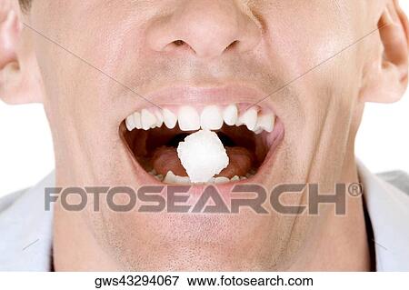 Stock Photo - Close-up of a young man holding a sugar cube between his teeth. Fotosearch