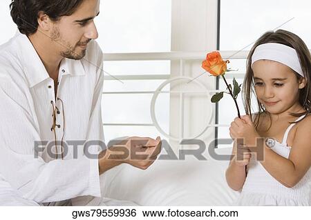 Close-up of a young man looking at his daughter holding a flower View Large Photo Image Stock Photograph - Close-up of a young man looking at his daughter holding a flower. Fotosearch