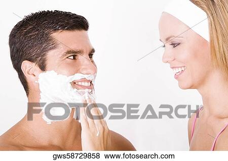 Stock Photo - Close-up of a young woman applying shaving cream on a mid adult man's face. Fotosearch