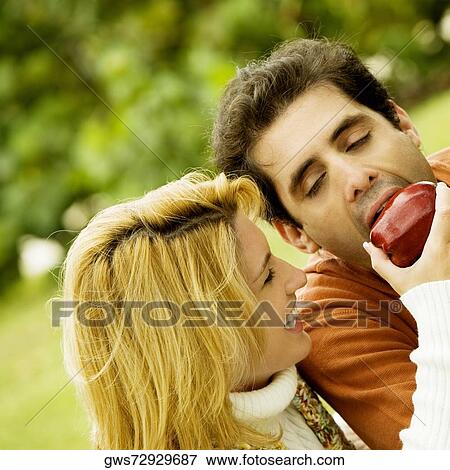 Close-up of a young woman feeding an apple to a mid adult man View Large Photo Image Stock Photo - Close-up of a young woman feeding an apple to a mid adult man. Fotosearch