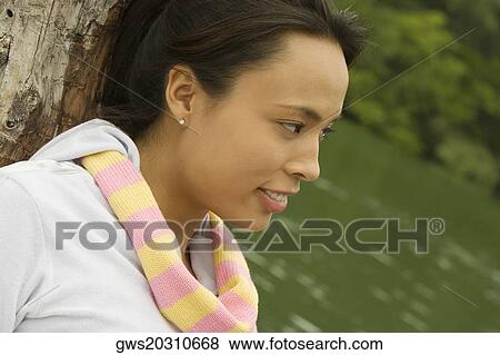 Close-up of a young woman leaning against a tree trunk View Large Photo Image Stock Photo - Close-up of a young woman leaning against a tree trunk. Fotosearch