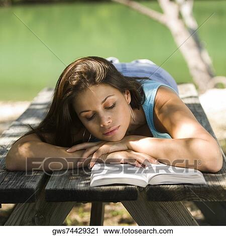 Stock Image - Close-up of a young woman lying on a bench reading a book. Fotosearch