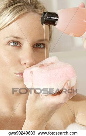 Stock Image - Close-up of a young woman pouring soap on a bath sponge. Fotosearch