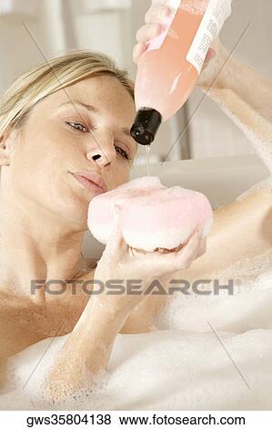 Stock Photo - Close-up of a young woman pouring soap on a bath sponge. Fotosearch