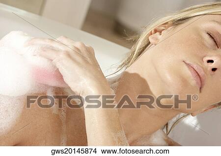 Close-up of a young woman scrubbing her shoulder with a bath sponge View Large Photo Image Picture - Close-up of a young woman scrubbing her shoulder with a bath sponge. Fotosearch