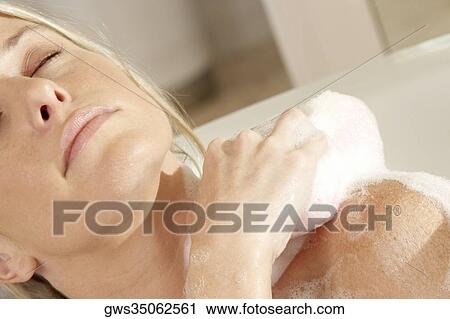 Stock Image - Close-up of a young woman scrubbing her shoulder with a bath sponge. Fotosearch