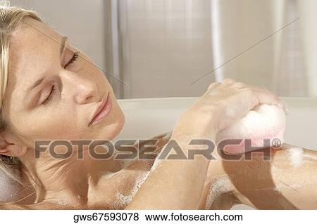 Close-up of a young woman scrubbing her shoulder with a bath sponge View Large Photo Image Stock Photo - Close-up of a young woman scrubbing her shoulder with a bath sponge. Fotosearch
