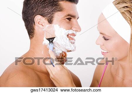 Picture - Close-up of a young woman shaving a mid adult man's face. Fotosearch