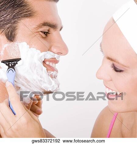 Stock Image - Close-up of a young woman shaving a mid adult man's face. Fotosearch