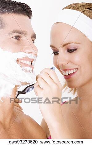Stock Image - Close-up of a young woman shaving a mid adult man's face. Fotosearch