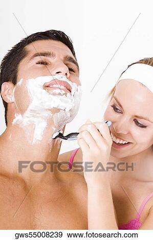 Stock Photo - Close-up of a young woman shaving a mid adult man's face. Fotosearch