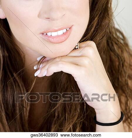 Stock Image - Close-up of a young woman smiling with her hand on her chin. Fotosearch