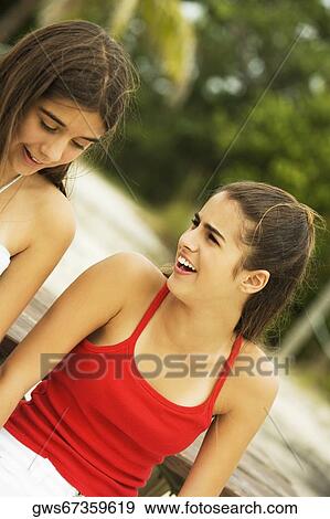 Stock Photo - Close-up of girl and a teenage girl sitting together smiling on the beach. Fotosearch