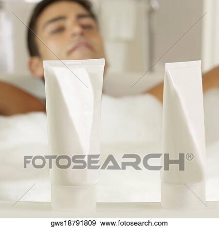 Close-up of two bottles of moisturizer with a young man in a bathtub behind it View Large Photo Image Stock Photo - Close-up of two bottles of moisturizer with a young man in a bathtub behind it. Fotosearch