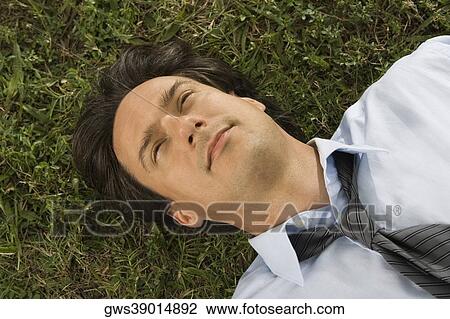 Stock Image - High angle view of a businessman lying on the grass. Fotosearch
