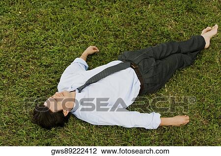 Stock Image - High angle view of a businessman lying on the grass. Fotosearch