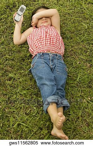High angle view of a girl lying on the grass holding a mobile phone View Large Photo Image Stock Photography - High angle view of a girl lying on the grass holding a mobile phone. Fotosearch