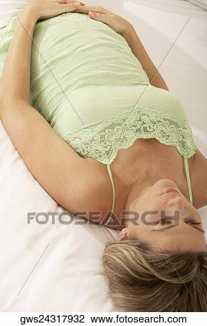 High angle view of a pregnant woman lying on the bed touching her abdomen View Large Photo Image Stock Image - High angle view of a pregnant woman lying on the bed touching her abdomen. Fotosearch