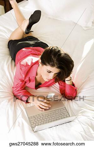 High angle view of a young woman lying on the bed using a laptop View Large Photo Image Stock Photo - High angle view of a young woman lying on the bed using a laptop. Fotosearch