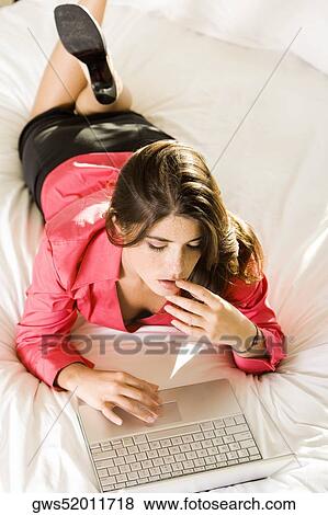 High angle view of a young woman lying on the bed using a laptop View Large Photo Image Stock Photo - High angle view of a young woman lying on the bed using a laptop. Fotosearch