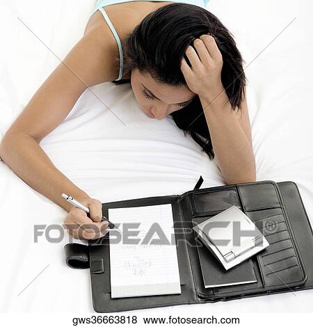 High angle view of a young woman writing in a note pad View Large Photo Image Stock Photo - High angle view of a young woman writing in a note pad. Fotosearch