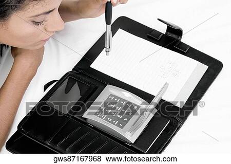 High angle view of a young woman looking at a calculator View Large Photo Image Stock Photo - High angle view of a young woman looking at a calculator. Fotosearch