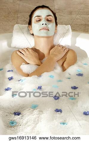Stock Photograph - High angle view of a young woman wearing a facial mask in a bathtub. Fotosearch