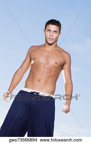Picture - Low angle view of a bare chested young man standing. Fotosearch