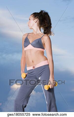 Stock Photography - Low angle view of a young woman holding dumbbells. Fotosearch