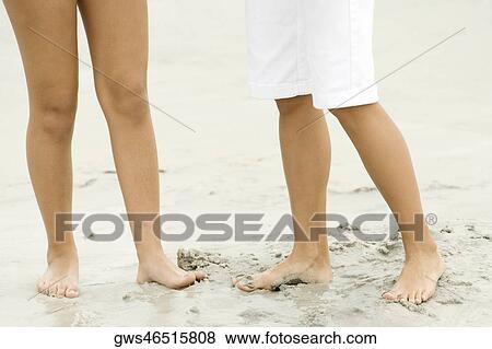 Stock Photo - Low section view of a man and a woman standing on the beach. Fotosearch