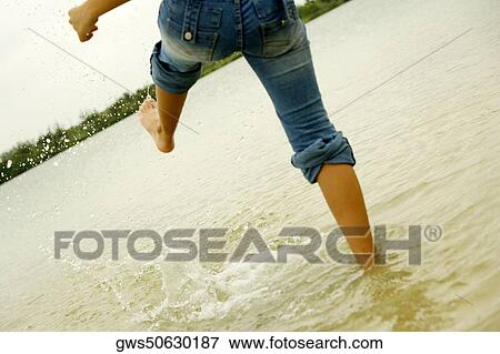 Stock Photo - Low section view of a woman kicking water on the beach. Fotosearch