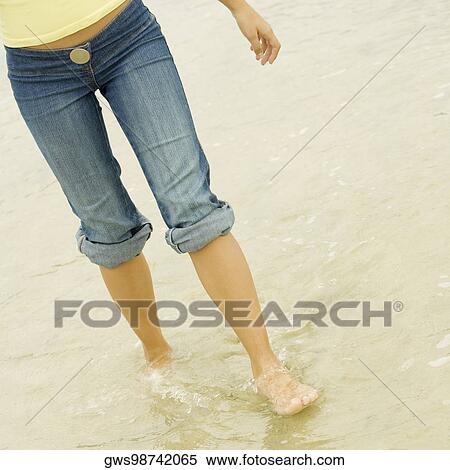 Stock Photography - Low section view of a young woman wading in water on the beach. Fotosearch