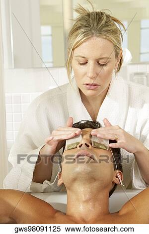 Stock Photography - Massage therapist putting teabags on a young man's eyes. Fotosearch