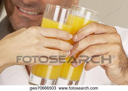 Stock Image - Mid adult man and a woman toasting with glasses of juice. Fotosearch