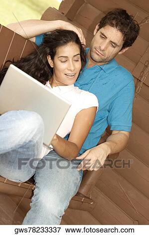Mid adult man and a young woman sitting on a porch swing with a laptop View Large Photo Image Stock Photo - Mid adult man and a young woman sitting on a porch swing with a laptop. Fotosearch