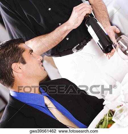 Mid adult man sitting at the table with a waiter showing him a wine bottle View Large Photo Image Stock Image - Mid adult man sitting at the table with a waiter showing him a wine bottle. Fotosearch