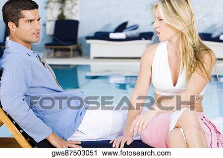 Stock Image - Mid adult man sitting with a young woman on a deck chair. Fotosearch