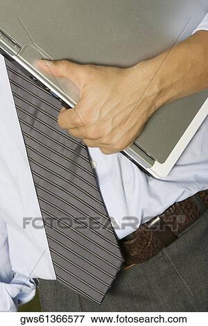 Mid section view of a man holding a laptop View Large Photo Image Stock Photo - Mid section view of a man holding a laptop. Fotosearch