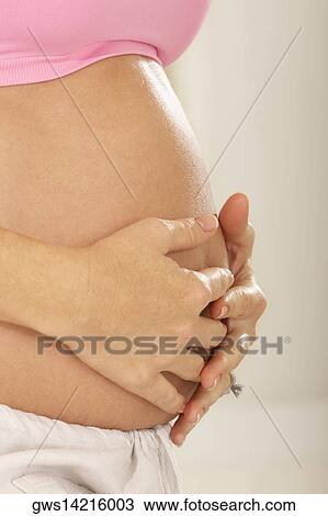 Stock Image - Mid section view of a pregnant woman touching her abdomen. Fotosearch