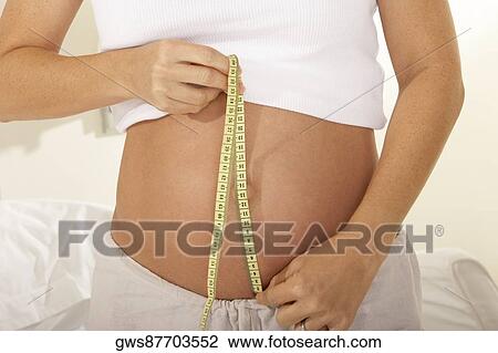 Mid section view of a pregnant woman measuring her abdomen with a measuring tape View Large Photo Image Stock Image - Mid section view of a pregnant woman measuring her abdomen with a measuring tape. Fotosearch