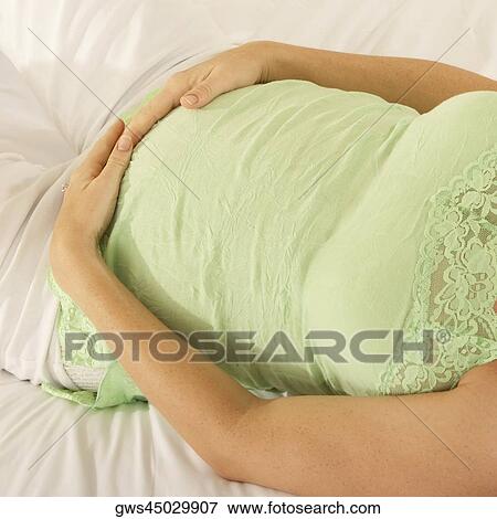 Mid section view of a pregnant woman lying on the bed touching her abdomen View Large Photo Image Stock Photo - Mid section view of a pregnant woman lying on the bed touching her abdomen. Fotosearch