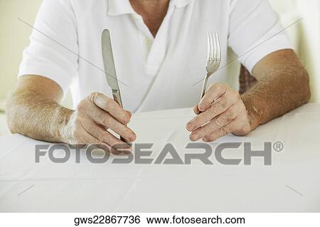 Stock Photograph - Mid section view of a senior man holding a table knife and a fork. Fotosearch
