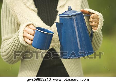 Stock Image - Mid section view of a woman holding a kettle and a mug. Fotosearch