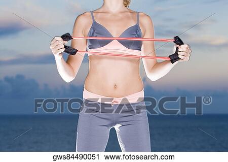 Stock Image - Mid section view of a young woman exercising with a resistance band. Fotosearch