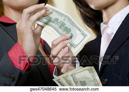 Stock Photography - Mid section view of two businesswomen holding dollar bills. Fotosearch