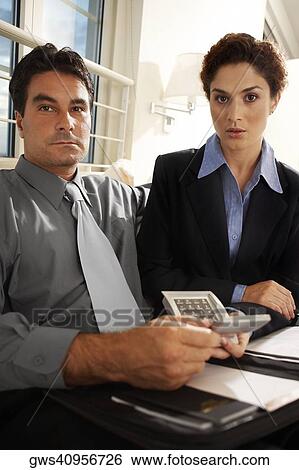 Portrait of a businessman sitting with a businesswoman holding a calculator View Large Photo Image Stock Photograph - Portrait of a businessman sitting with a businesswoman holding a calculator. Fotosearch