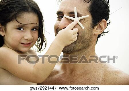 Portrait of a girl covering her father's eye with a starfish View Large Photo Image Stock Photo - Portrait of a girl covering her father's eye with a starfish. Fotosearch