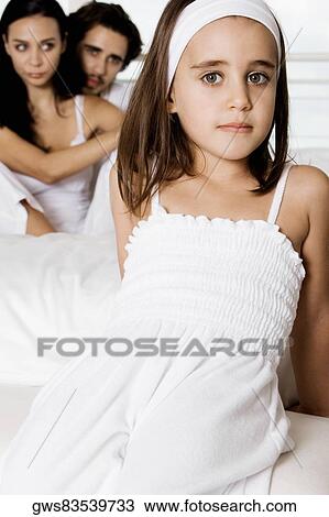 Portrait of a girl reclining on the bed with her parents sitting behind her View Large Photo Image Stock Image - Portrait of a girl reclining on the bed with her parents sitting behind her. Fotosearch