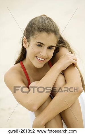 Stock Image - Portrait of a girl sitting on the beach smiling. Fotosearch